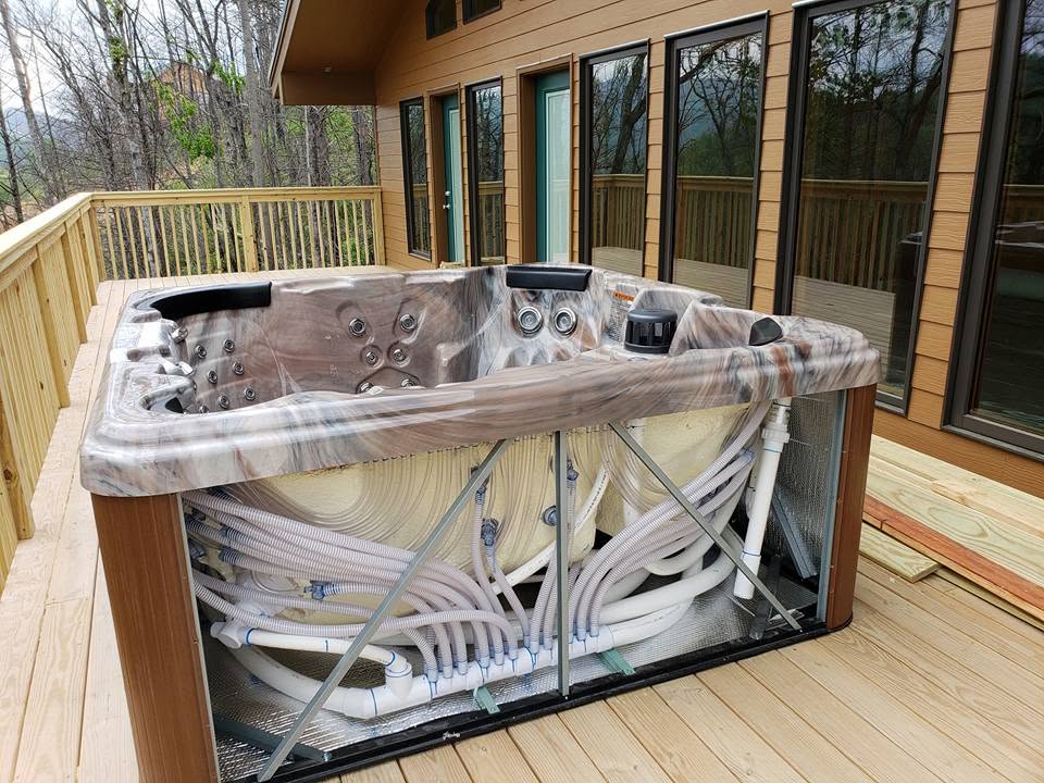 Hot tub on a cabin deck with its side panel removed and plumbing exposed for on-site repair
