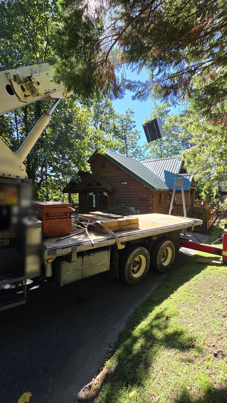 Boom truck lifting a hot tub over a log cabin surrounded by trees