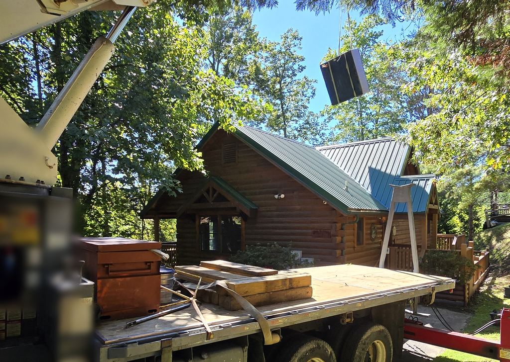 Boom truck crane lifting a hot tub toward a log cabin in the trees
