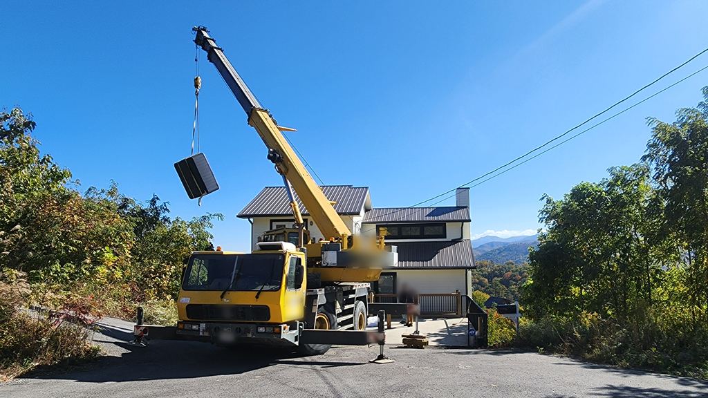 Yellow crane truck lifting a hot tub high over a mountain home on a clear blue day
