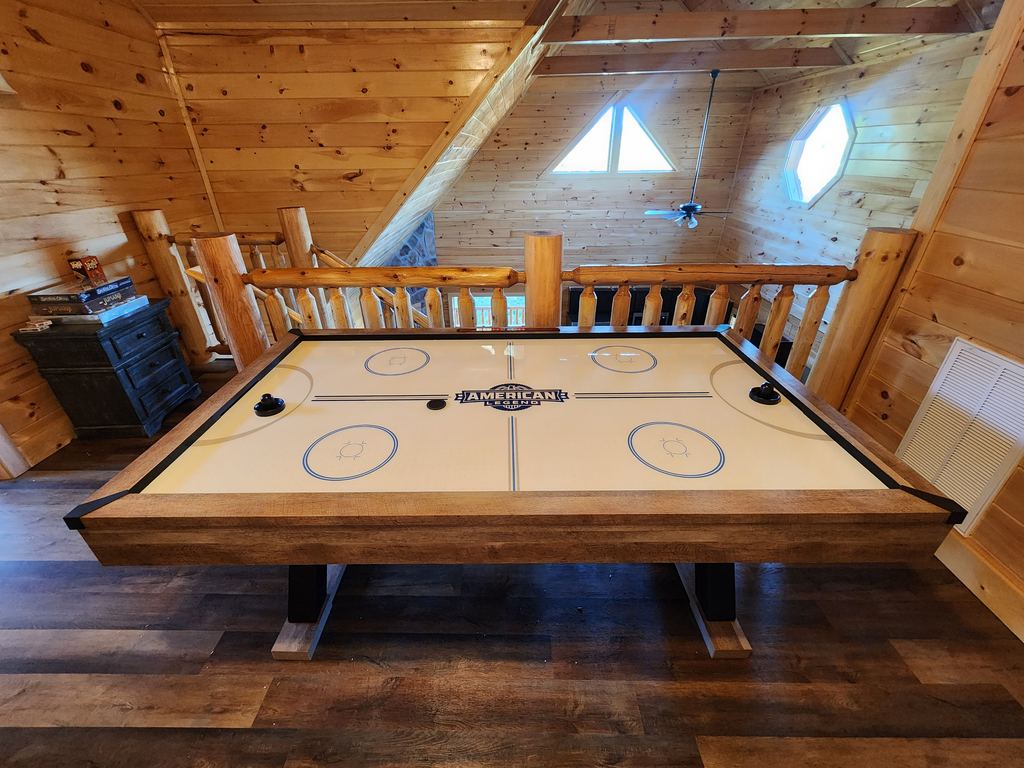 Full-size air hockey table set up in a log cabin loft game room