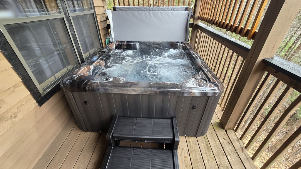 New hot tub with a marbled shell and the jets running on a covered cabin deck, with steps and the cover lifted
