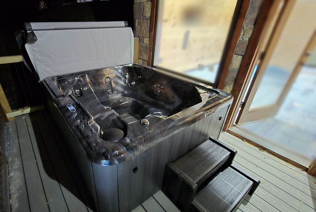 Newly installed hot tub on a cabin deck at night, with a gray cabinet, steps and the cover lifted