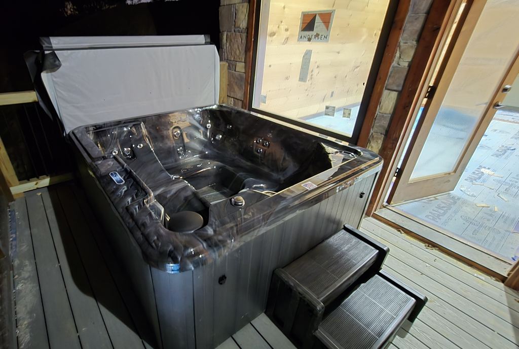 Newly installed hot tub on a cabin deck at night, with a gray cabinet, steps and the cover lifted