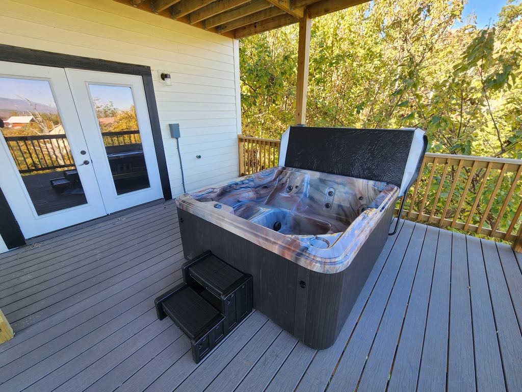 Hot tub with a marbled shell and steps on a gray composite deck by French doors