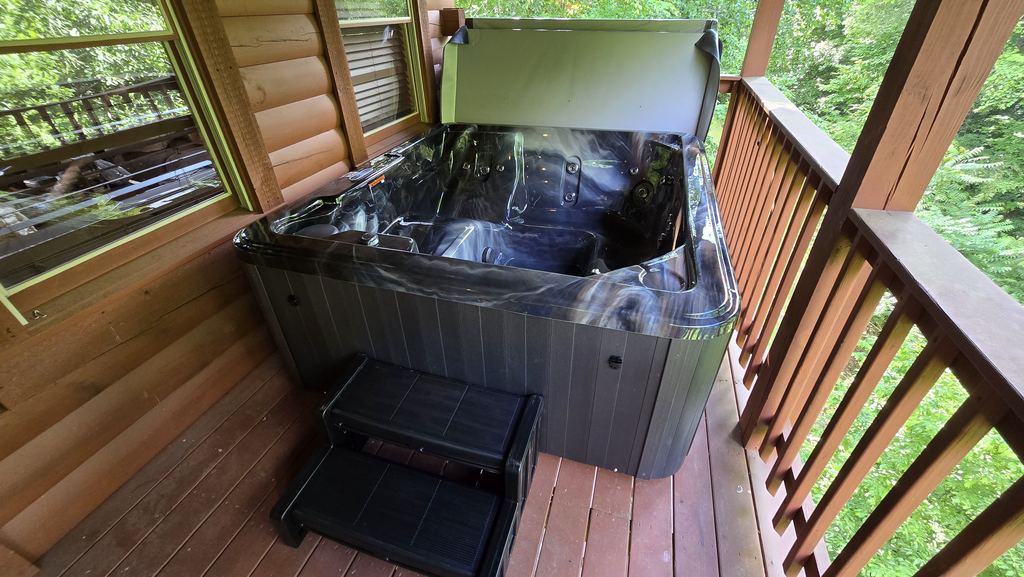 Hot tub with the cover lifted and steps on a covered cabin porch