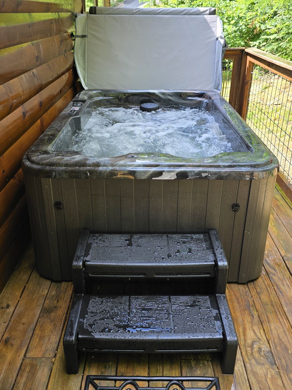 Hot tub with steps and the jets running on a covered cabin porch
