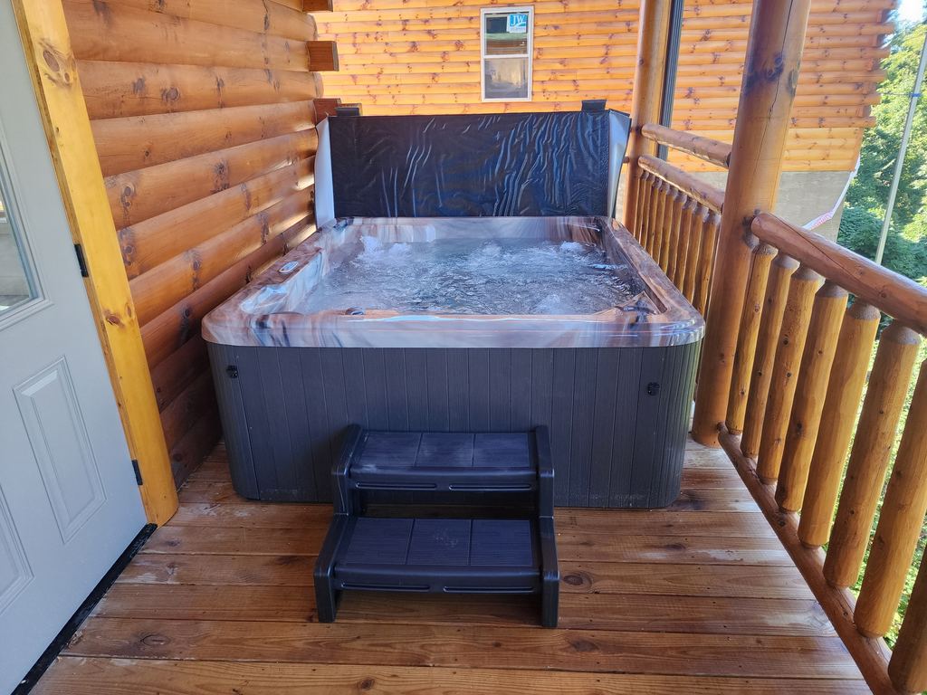 Hot tub with steps on a covered log cabin porch beside the door
