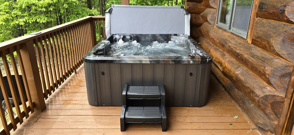 Hot tub with the jets running and steps on a log cabin deck in the woods