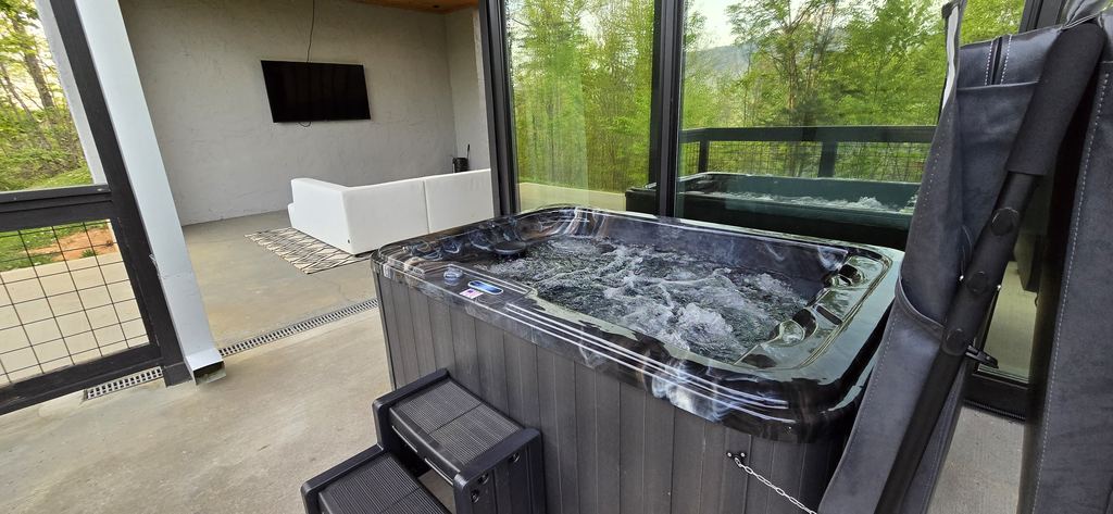 Hot tub with steps on a modern cabin patio beside glass doors