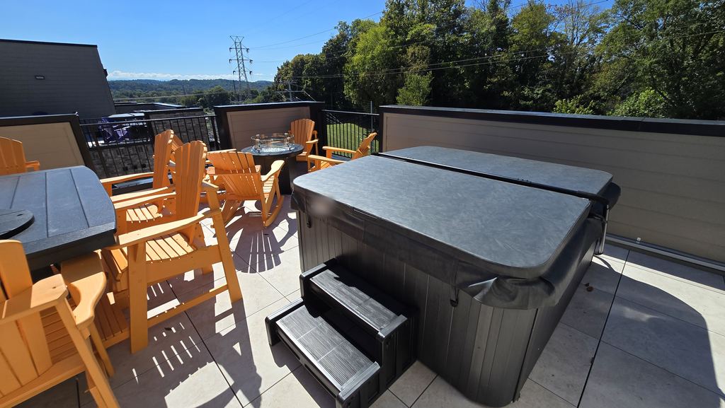 Covered hot tub with steps on a sunny rooftop patio next to orange Adirondack chairs
