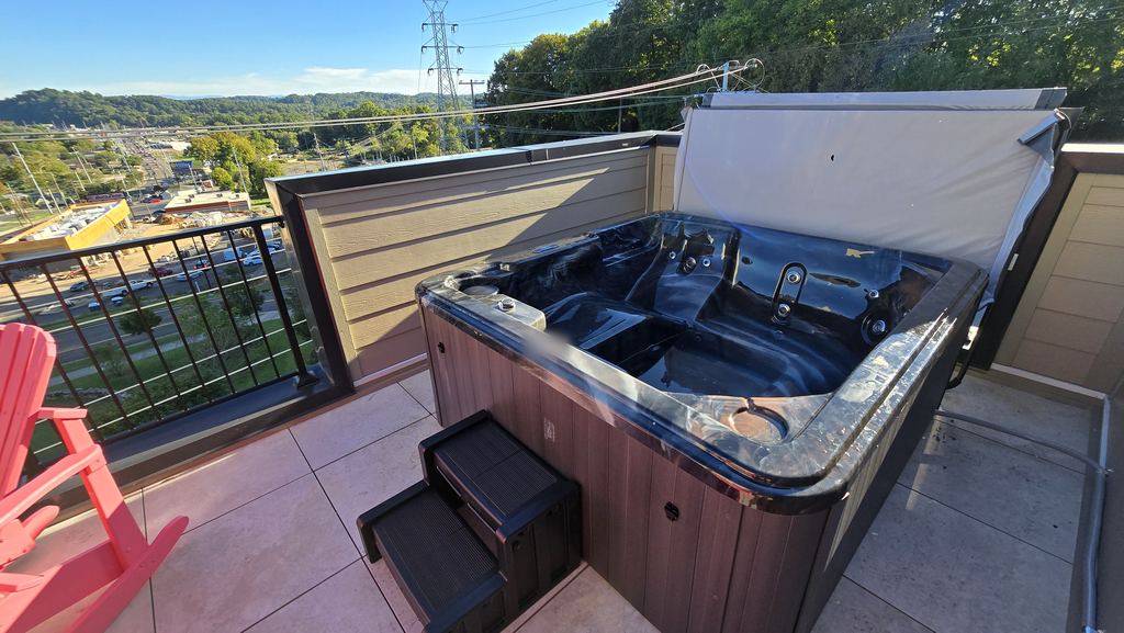 Rooftop hot tub with steps and a brown cabinet, with hills and trees in the distance