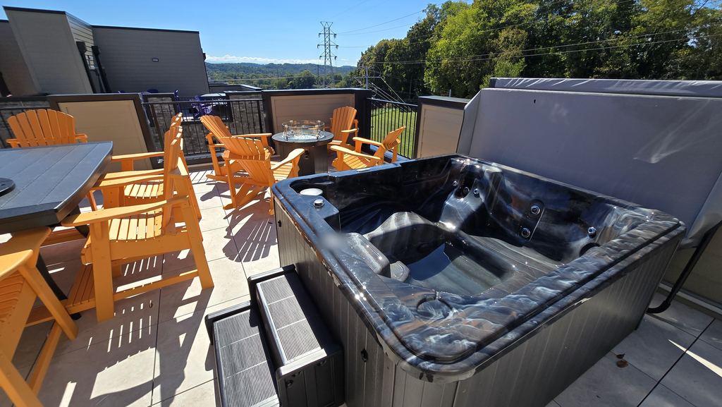 New hot tub with the cover lifted on a sunny rooftop patio, with steps and orange Adirondack chairs around a fire table