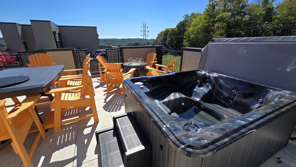 Closer view of a rooftop hot tub with steps, orange Adirondack chairs and a fire table behind it
