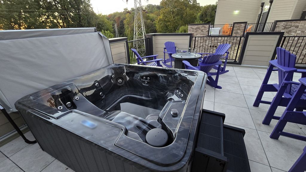 Close view of a rooftop hot tub with a lit topside control, steps and purple chairs at sunset