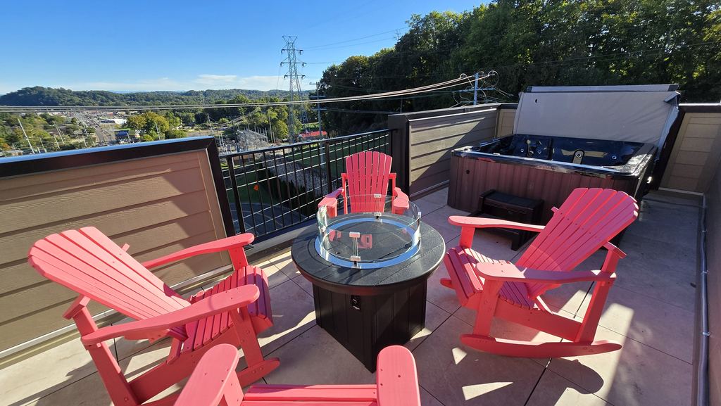 Rooftop patio with red Adirondack chairs around a fire table and a hot tub behind them