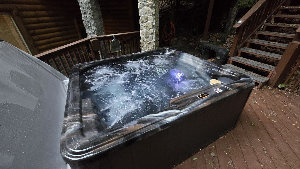 Hot tub with its LED light on and the jets running on a wooded cabin deck