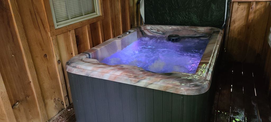 Hot tub glowing purple from its LED light on a covered wooden porch