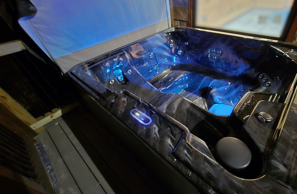 Hot tub with the cover lifted and blue underwater lights on, set on a covered cabin deck