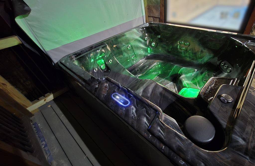 The same hot tub glowing green under its lifted cover on a cabin deck