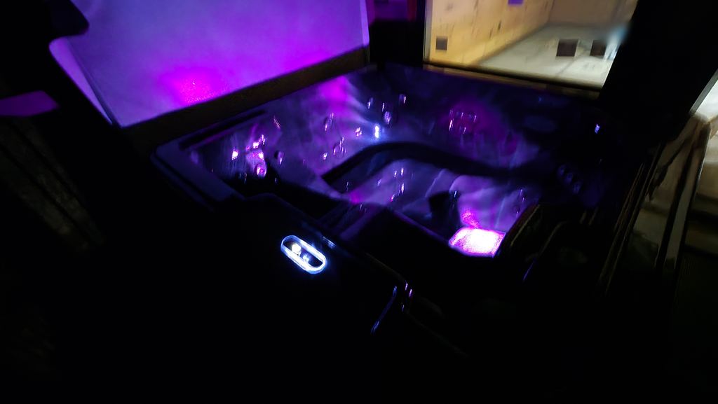 Hot tub at night with purple underwater lights and a glowing topside control