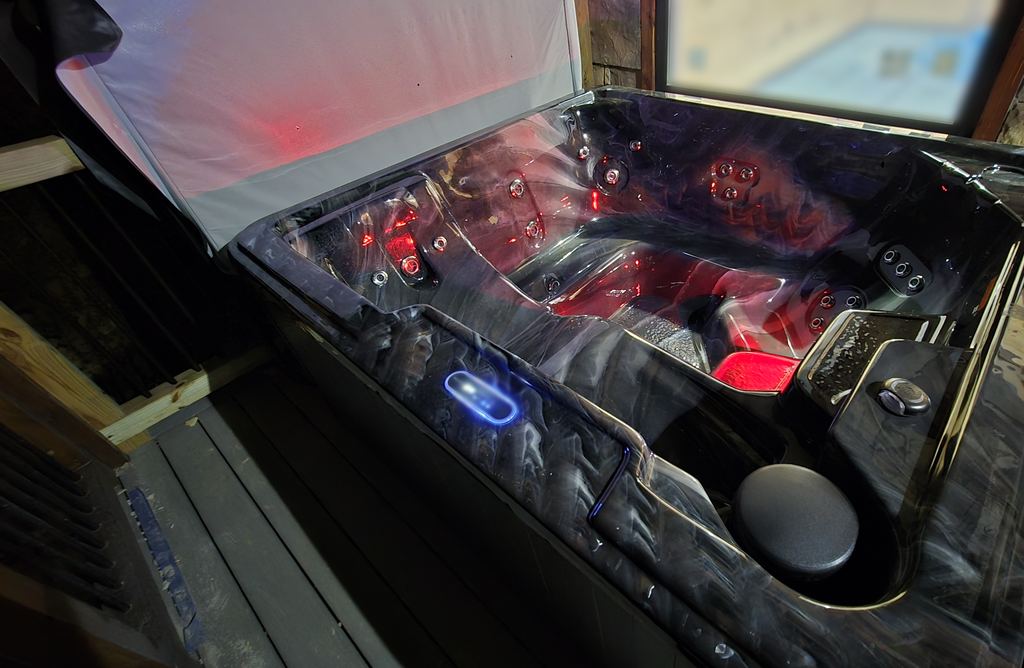 The same hot tub with its underwater lights set to red, cover lifted on a cabin deck