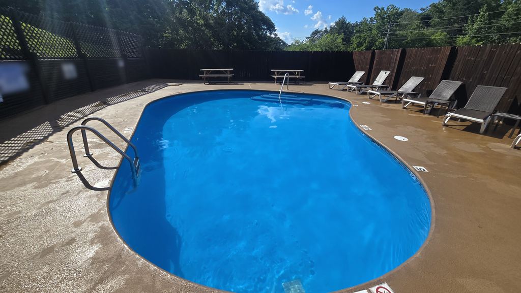 Clear blue community pool with a ladder, picnic tables and lounge chairs along a privacy fence