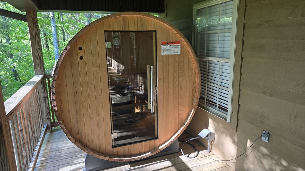 Cedar barrel sauna with a glass door on a covered cabin porch
