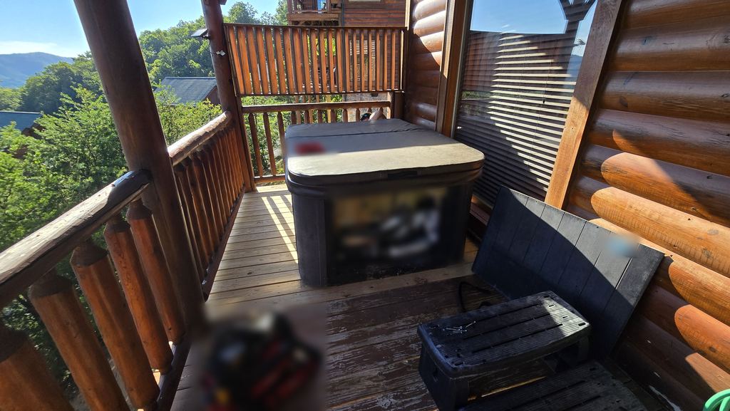 Hot tub on a log cabin deck with the equipment panel open for service and a tool bag nearby